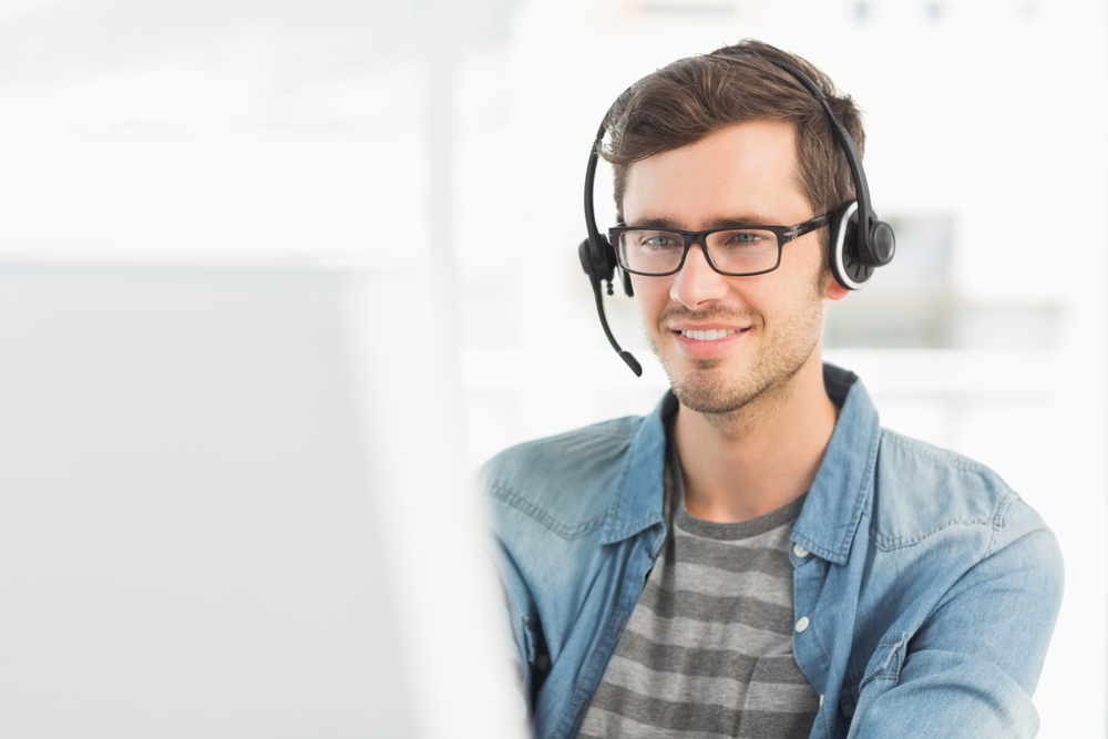 Smiling casual young man with headset using computer in a bright office Smiling casual young man with headset using computer in a bright office